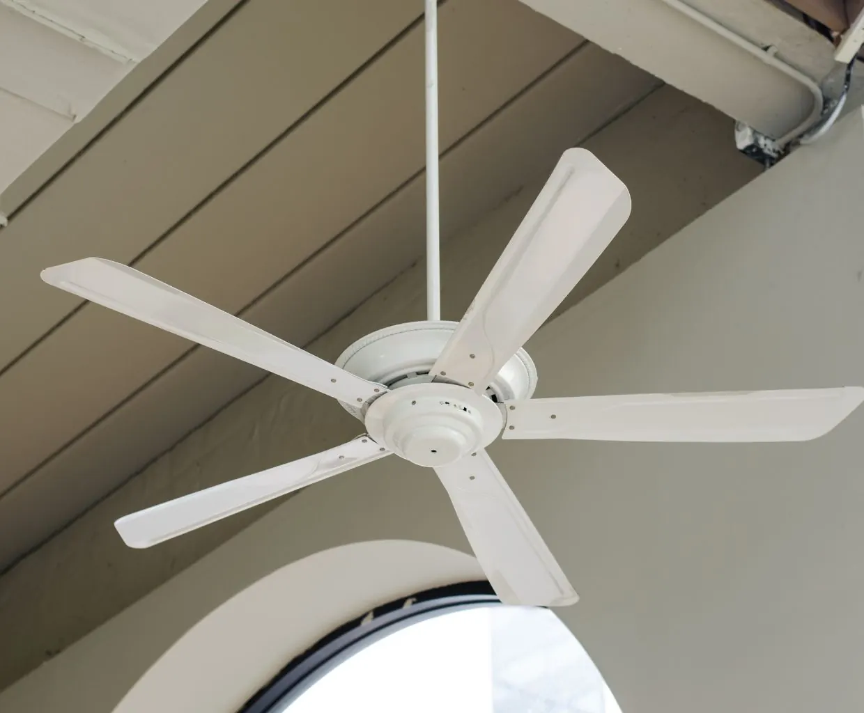 White five-blade ceiling fan on a long downrod under a sloped porch ceiling, above an arched window