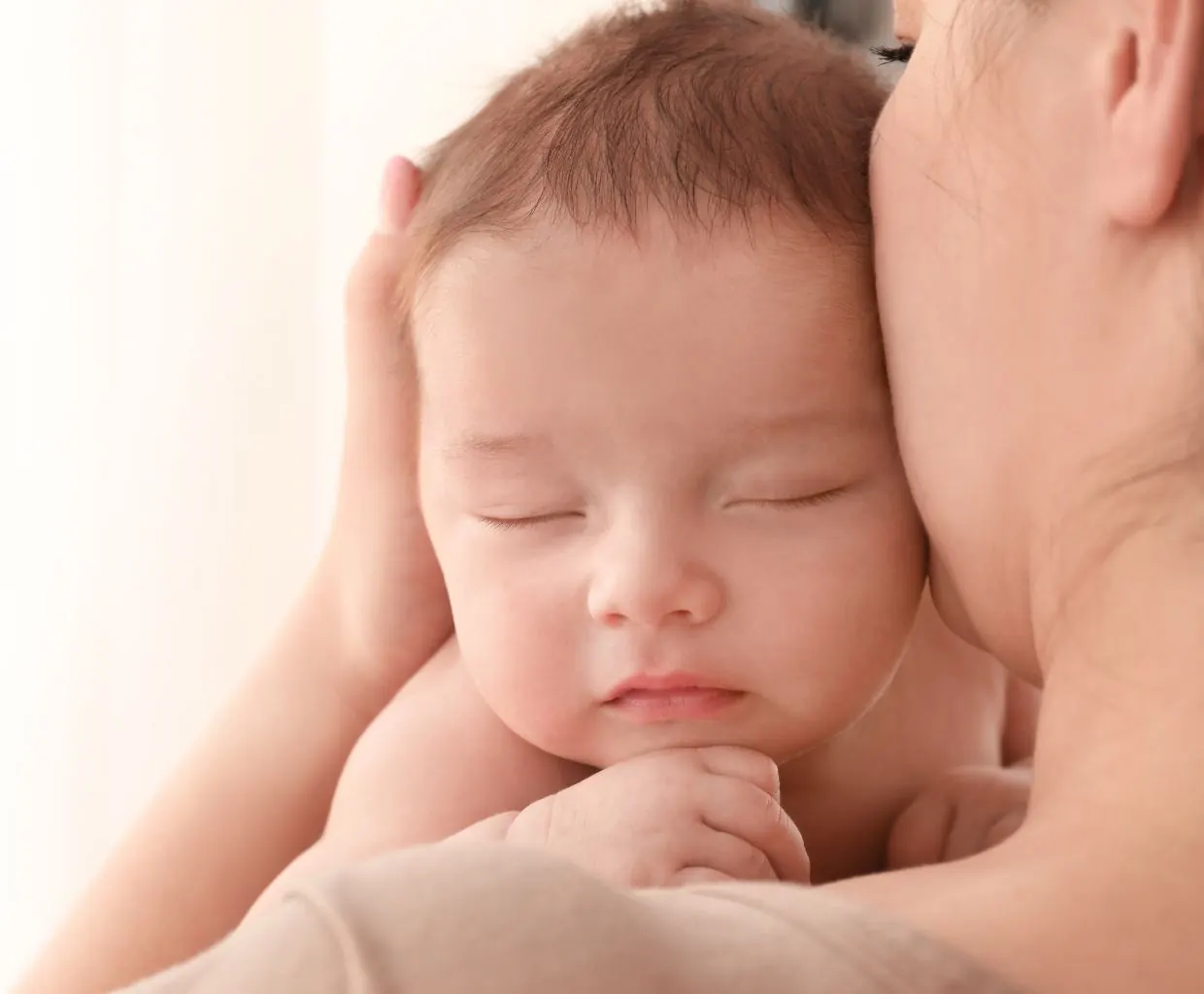 Sleeping baby resting against a parent's shoulder, with the parent's hand cradling the baby's head