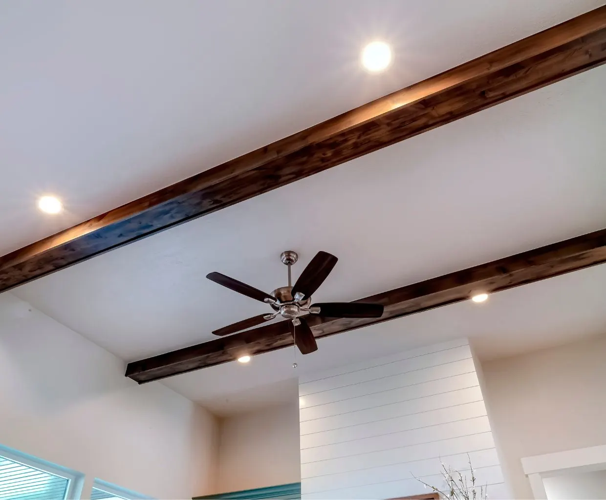 Dark ceiling fan on a high white ceiling crossed by exposed dark wood beams