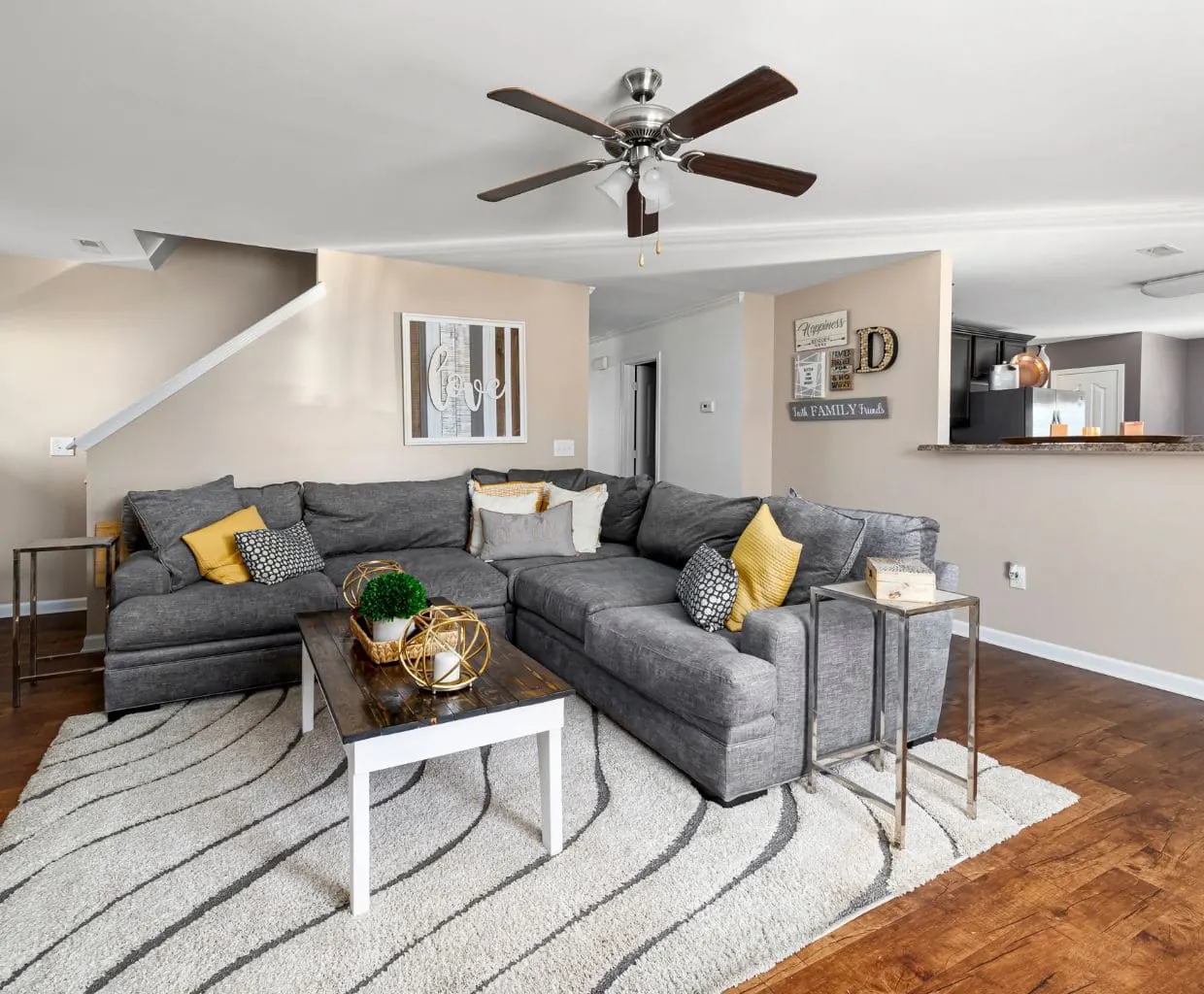 Living room with a gray sectional sofa under a five-blade ceiling fan with dark wood blades and a light kit