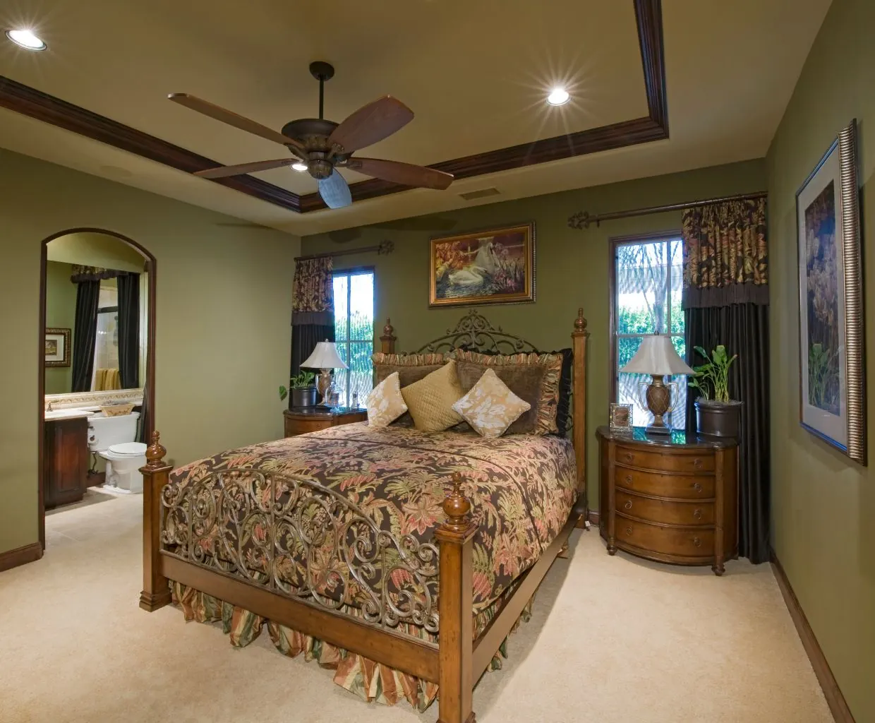 Bedroom with olive walls, a wood and wrought-iron bed and a five-blade wood ceiling fan in a tray ceiling